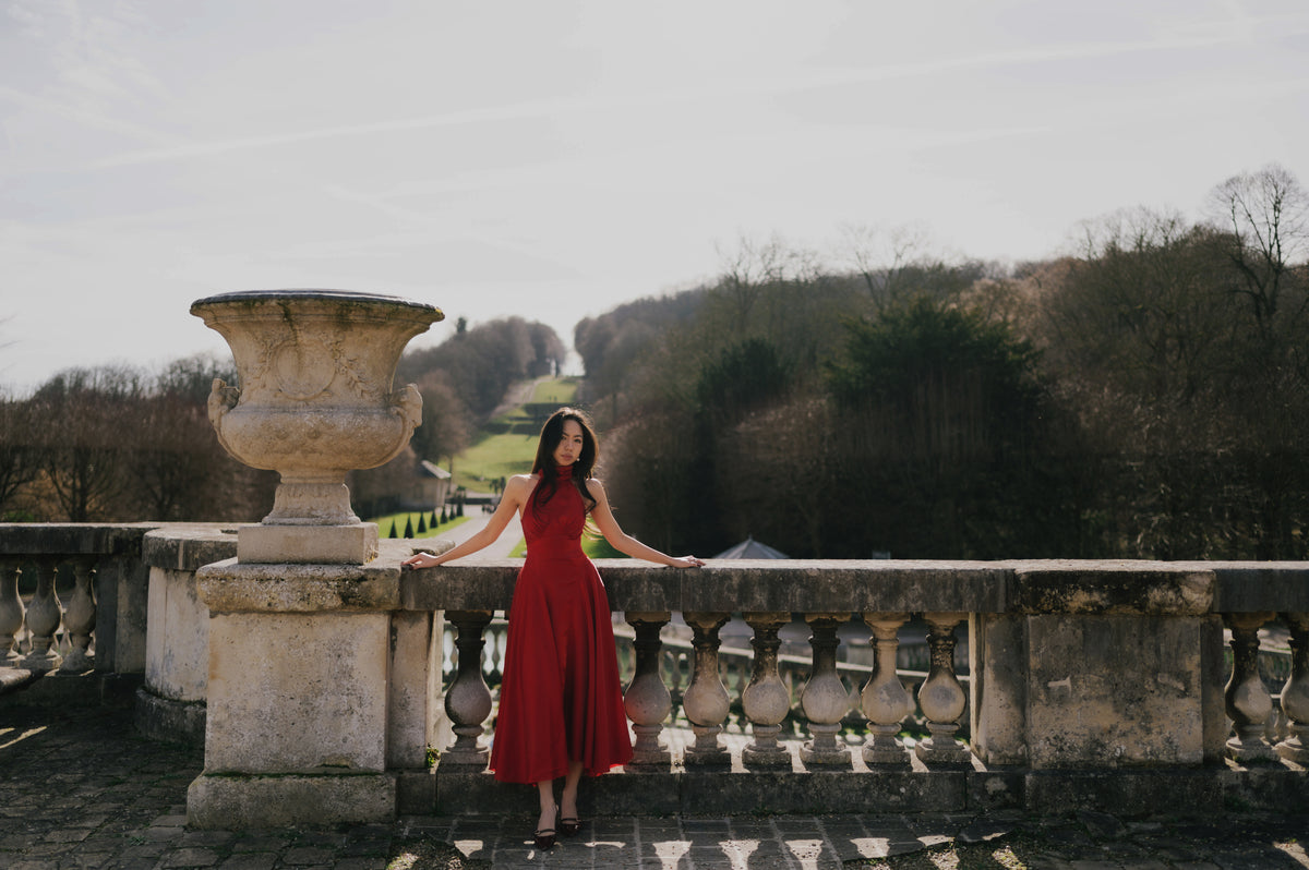 Lizzie in a red dress leaning on a stone balustrade in a park